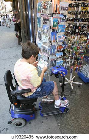 Stock Photography - Boy using a scooter/cart purchasing a post card on the streets of New York City.. Fotosearch