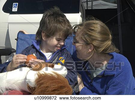 Stock Image - Boy (wheelchair user with ball & stuffed animal) with autism and Mom sharing a laugh. Fotosearch