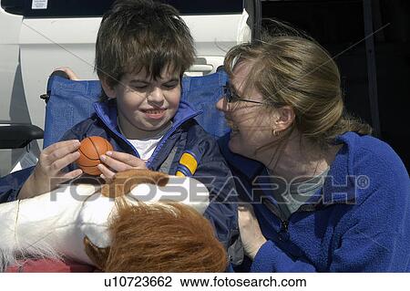 Stock Image - Boy (with autism) in wheelchair shares a laugh with Mom. Fotosearch