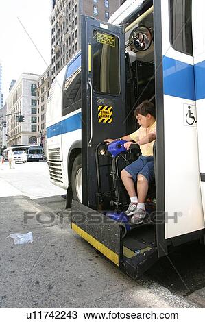 Stock Image - Boy with Muscular Dystrophy, utilizing a scooter/cart for mobility, exiting a city bus via a chair lift.. Fotosearch