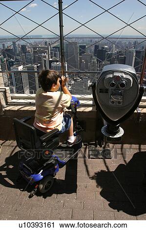 Stock Image - Child with Muscular Dystrophy utilizing a scooter/cart for mobility using a viewer while enjoying a trip to the city.. Fotosearch