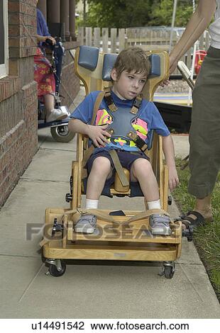 Stock Image - Child with severe physical disabilities utilizing a custom designed positioning chair.. Fotosearch