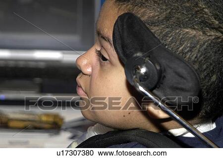 Stock Image - Little boy with significant disabilities utilizing a wheelchair with headgear for positioning and mobility.. Fotosearch