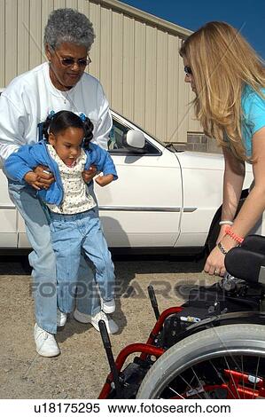 Little girl with a disability receiving assistance from her grandmother and an aide to get into her wheelchair. View Large Photo Image Stock Photography - Little girl with a disability receiving assistance from her grandmother and an aide to get into her wheelchair.. Fotosearch