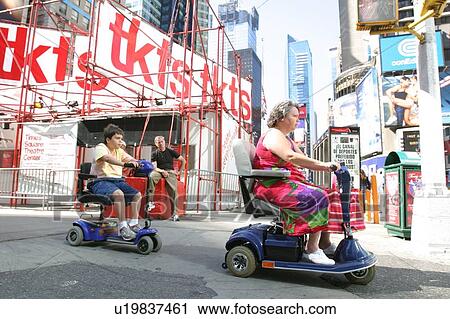 Stock Image - Mother and son crossing a street in New York City, using scooters/carts, while vacationing there.. Fotosearch
