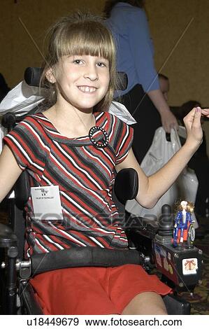 Stock Photo - Smiling girl utilizing a powered wheelchair for mobility with a wheelchair Barbie on her chair.. Fotosearch