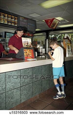 Stock Image - Little boy with multiple disabilities, including blindness, using a braille menu to place an order at a fast food restaurant.. Fotosearch