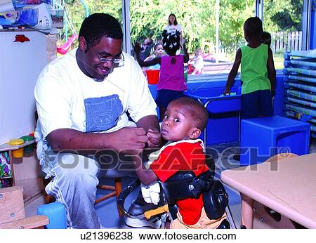 Stock Photo - Precious little boy with disabilities interacting with his occupational therapist while at his developmental day program.. Fotosearch