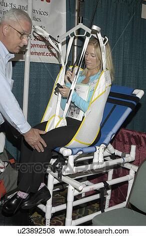 Woman with a physical disability sitting in and testing bathing lift and transfer equipment while a man assists her by positing her legs in the lift. View Large Photo Image Stock Photo - Woman with a physical disability sitting in and testing bathing lift and transfer equipment while a man assists her by positing her legs in the lift.. Fotosearch
