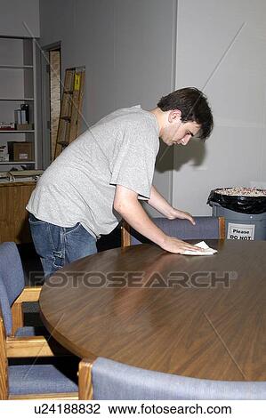 Stock Image - A man with a disability is working in an office cleaning a conference table.. Fotosearch