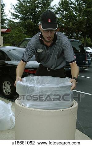 Stock Image - Close up of a man emptying a commercial trash can.. Fotosearch