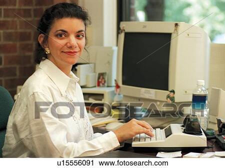Stock Image - Woman who is deaf using a TTY or TDD device to communicate with clients on the telephone at her job.. Fotosearch
