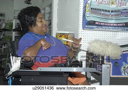 Woman with a disability, utilizing a wheelchair for mobility, working in a video store. View Large Photo Image Stock Photograph - Woman with a disability, utilizing a wheelchair for mobility, working in a video store.. Fotosearch