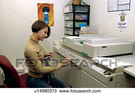 Stock Image - Woman with a disability, utilizing crutches to assist with mobility, making copies of documents as a part of her daily duties at work.. Fotosearch
