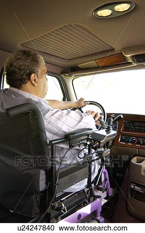 Stock Image - Man utilizing a wheelchair for mobility driving a van modified with hand controls.. Fotosearch