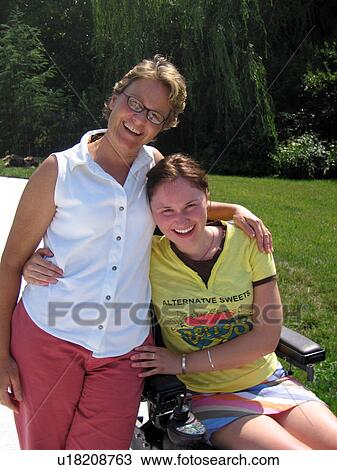Stock Image - Mother and daughter (seated in electric wheelchair) share a hug for the cameraman.. Fotosearch