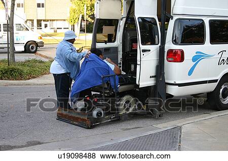 Stock Photo - Person in a wheelchair receiving assistance in using a lift as he prepares to get into a van.. Fotosearch