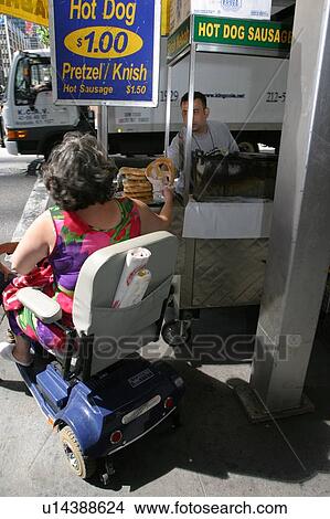 Woman using a scooter buying a hot dog from a street vendor. View Large Photo Image Picture - Woman using a scooter buying a hot dog from a street vendor.. Fotosearch