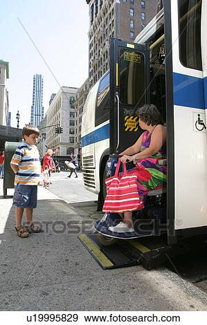 Stock Photo - Woman using a scooter/cart for mobility leaving a city bus via a lift.. Fotosearch