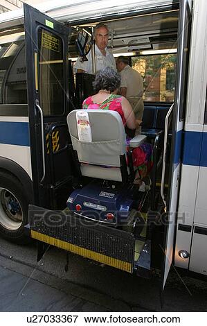 Stock Photo - Woman using a scooter/cart for mobility getting on a city bus via a lift.. Fotosearch