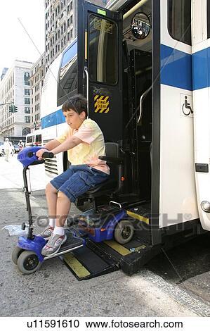Stock Image - Boy with Muscular Dystrophy, utilizing a scooter/cart for mobility, exiting a city bus via a chair lift.. Fotosearch