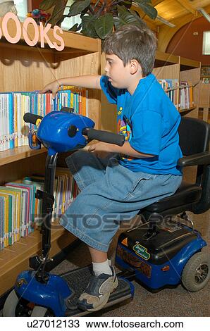 Boy with Muscular Dystrophy, utilizing a scooter/cart for mobility, selecting a book to check-out from the school library. View Large Photo Image Stock Image - Boy with Muscular Dystrophy, utilizing a scooter/cart for mobility, selecting a book to check-out from the school library.. Fotosearch