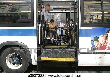 Stock Image - Boy with Muscular Dystrophy, utilizing a scooter/cart for mobility, using a city bus via a chair lift.. Fotosearch