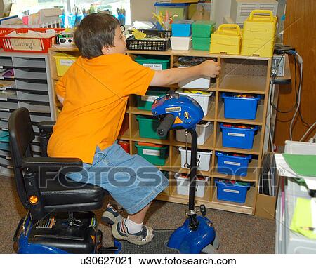 Boy with Muscular Dystrophy, utilizing a scooter/cart for mobility, reaching for a bin of art supplies. View Large Photo Image Stock Image - Boy with Muscular Dystrophy, utilizing a scooter/cart for mobility, reaching for a bin of art supplies.. Fotosearch
