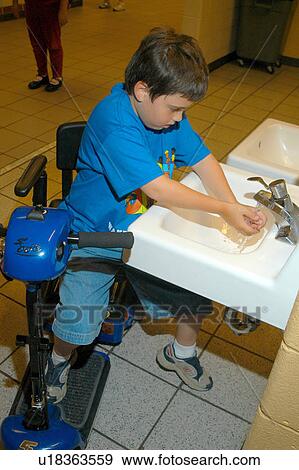 Stock Photo - Boy with Muscular Dystrophy, utilizing a scooter/cart for mobility, washing his hands in the restroom.. Fotosearch