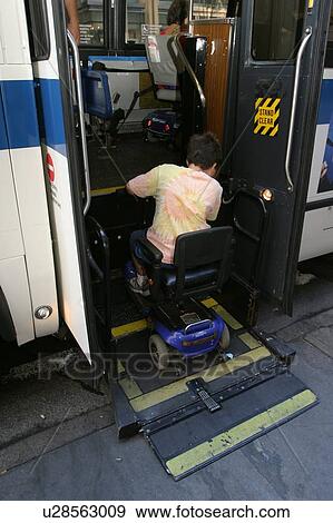 Stock Photo - Boy with Muscular Dystrophy, utilizing a scooter/cart for mobility, getting on a city bus via a chair lift.. Fotosearch