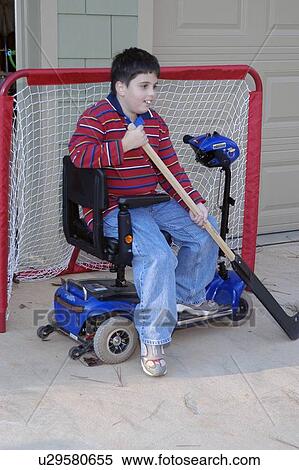Stock Photography - Boy with Muscular Dystrophy, utilizing a scooter for mobility, playing a game of street hockey.. Fotosearch