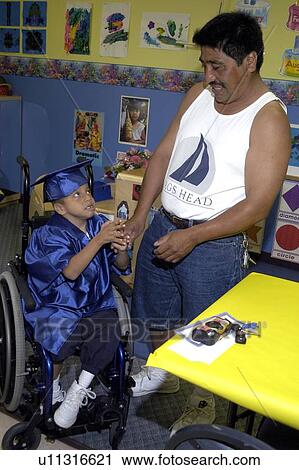 Stock Image - Father and son sharing a moment together prior to graduation ceremonies. The ôgraduateö has multiple disabilities.. Fotosearch