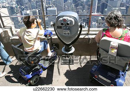 Stock Image - Mom and son, both using scooters for mobility, sight seeing on vacation.. Fotosearch