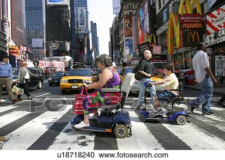 Stock Image - Mother and son crossing a street in New York City, using scooters/carts, while vacationing there.. Fotosearch