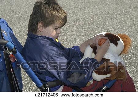 Stock Photograph - Side shot of a boy (autistic) in a wheelchair playing with toys. Fotosearch