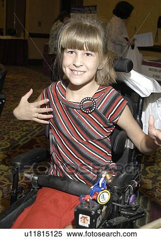 Stock Photography - Smiling girl utilizing a powered wheelchair for mobility with a wheelchair Barbie on her chair.. Fotosearch