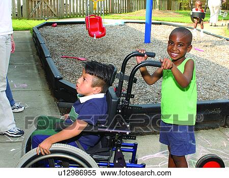 Two adorable little boys playing on the playground. The child without a disability is giving his friend who uses a wheelchair some assistance to get from one place to another. View Large Photo Image Stock Photography - Two adorable little boys playing on the playground. The child without a disability is giving his friend who uses a wheelchair some assistance to get from one place to another.. Fotosearch