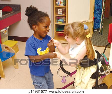 Stock Photo - Absolutely adorable image of two friends, one with multiple disabilities, one with none, interacting in a classic little girl game as they play together at school.. Fotosearch
