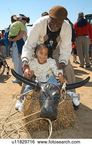 Stock Photograph - Adorable little girl with multiple disabilities riding a pretend bull with help from her grandfather.. Fotosearch