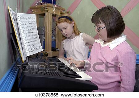 Stock Photography - Girl with Down Syndrome playing the piano/keyboard with sister watching.. Fotosearch