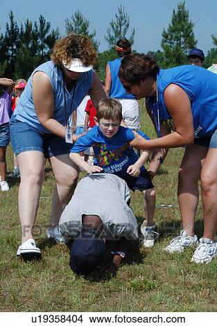 Picture - Little boy with disabilities receiving a couple of helping hands to play leap frog with his friends.. Fotosearch