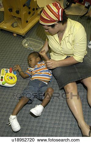 Stock Image - Little boy with severe physical disabilities playing on the floor with the assistance of a care provider.. Fotosearch
