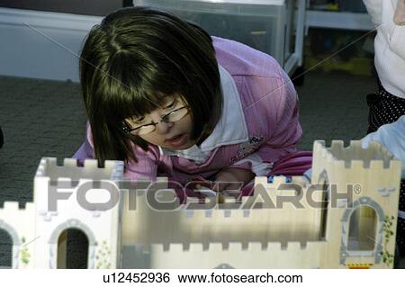 Stock Photograph - Little girl with Down Syndrome playing with a castle.. Fotosearch