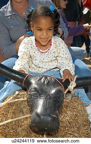 Little girl with multiple disabilities riding a pretend bull at a fun family outing. View Large Photo Image Stock Photo - Little girl with multiple disabilities riding a pretend bull at a fun family outing.. Fotosearch