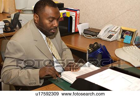 Stock Photo - Man with a disability who utilizes a wheelchair for mobility working at his desk.. Fotosearch