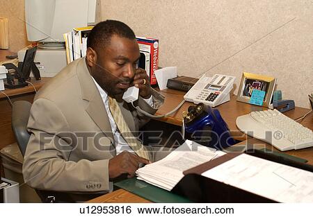Stock Photograph - Man with a disability who utilizes a wheelchair for mobility working at his desk and talking on the telephone.. Fotosearch