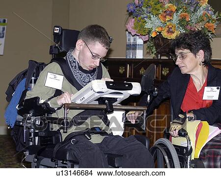 Picture - A young man with cerebral palsy sitting in a wheelchair using a speech device to communicate with a woman in a wheelchair.. Fotosearch