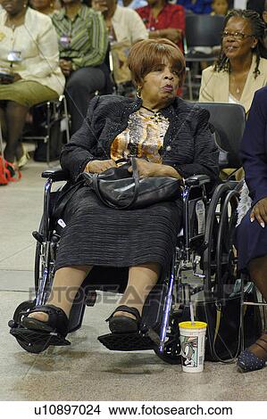 Picture - Elderly African American woman with physical disabilities sitting in her wheelchair while participating in a meeting at an auditorium.. Fotosearch