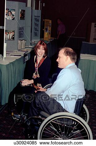 Stock Photography - Man and woman, both with disabilities, both utilizing wheelchairs for mobility, chatting and having a good time while viewing exhibits.. Fotosearch