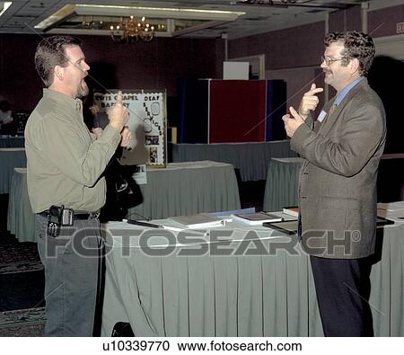 Stock Image - Man who is deaf and blind (on left) talking via American Sign Language with an interpreter at an event.. Fotosearch